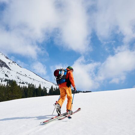 Ski mountaineer walking up along a snowy ridge with the skis in the backpack. In background a blue sky. Snow and winter activities, skitouring in mountains.の写真素材