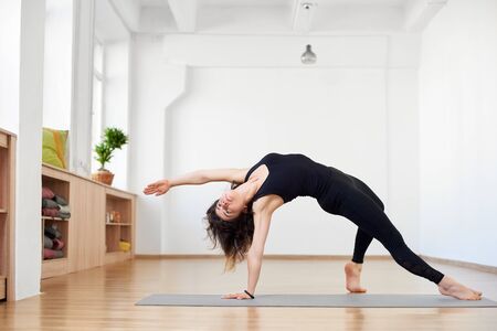 Fit sporty flexible girl doing backbend stretching exercise. Camatkarasana Wild Thing or Flip-the-Dog pose. Black and white view. Copy space on top on white background. Grace, beauty, strength, healthの写真素材
