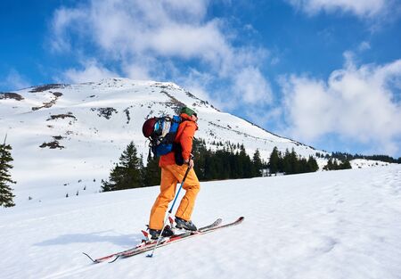 Mountaineer walking up along a snowy ridge with the skis in the backpack at sunny day. In background the peaks of mountains at sunny day. Snow and winter activities, skitouring in mountains.の写真素材