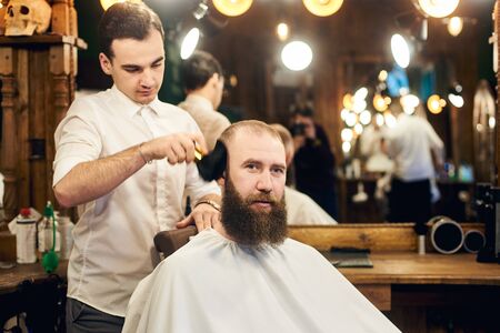 Barber shaking off hair remnants with brush for taking care of clients face in barbershop. Coiffeur finishing haircutting. Final stage of customer service in professional hairdressing salon for men.の写真素材