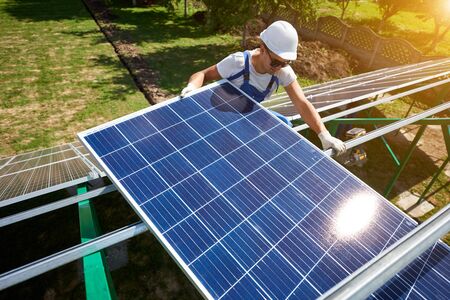 Young smiling mounter installing modern solar panels on green metallic carcass. Innovative electricity resources technologies. Ecological friendly, nature saving, economical. Renewable energy.の写真素材