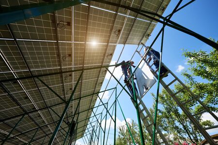 Mounting solar batteries during sunny day by professinal workers. Installing solar panels on high metallic construction. Environment friendly, green energy. Ecological. Using natural renewable energy.の写真素材