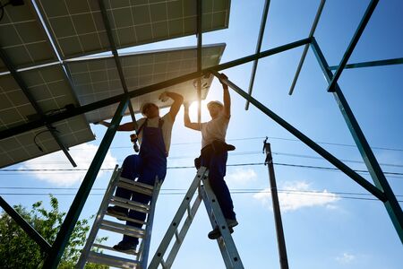 Working hard: solar panels on metallic carcass mounting. Two workers keeping solar battery. Modern...