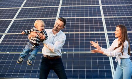 Happy young family with a little blond child having fun on the background of solar panels. A modern world with continuously advancing technologyの写真素材