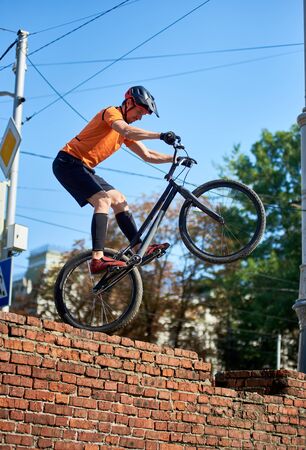 Side view of guy in black shorts stands on one wheel of a sports bike. Serious man cycling in city on nature background. Concept of sport.の写真素材