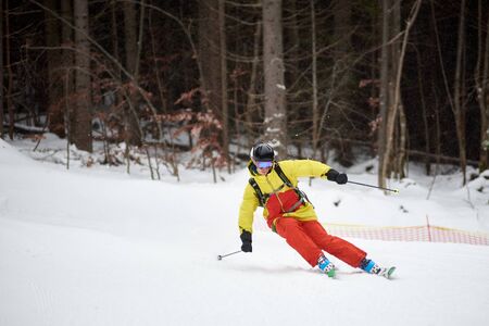 Sporty skier performing skiing trick. Ski training during snowfall. Carving skiing technique. Tall trunks of trees and dark forest on background. Winter activities, freestyle, adventure conceptの写真素材