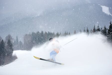 Invisible skier jumping high up in deep snow powder. Skiing in blizzard. Dark wooded mountain landscape in snowfall on background. Danger, overcoming obstacles, hardening, struggle, endurance.の写真素材