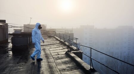 Scientist wearing white protective coverall and gas mask, walking on the roof of an urban building....