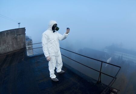 Fisheye snapshot of a researcher in a protective suit and a gas mask, who is working in a potentially dangerous exclusion zone, studing content of flaskの写真素材