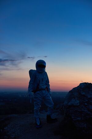 Vertical shot of astronaut silhouette standing on rocky mountain during sunset. Cosmonaut wearing...