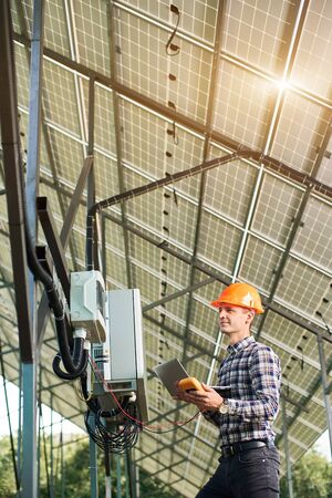 Checking the operation of solar power station. Man in helmet and with laptop and sensor in his hands. Science technology. Global warming. Green energy.の写真素材