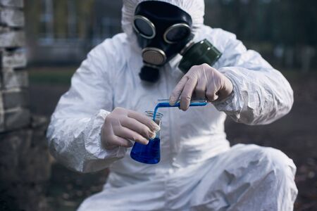 Cropped, close-up snapshot of a scientist in protective suit, gas mask and gloves, making expertise...
