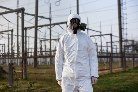Scientist wearing white protective uniform, gas mask and gloves on the territory of thermal power...