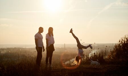 Mother and father are standing on the hill and watching their daughter doing a handstand, behind...