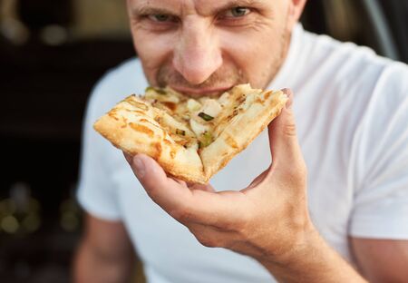 Close up view of hungry man eating piece of pizzaの写真素材