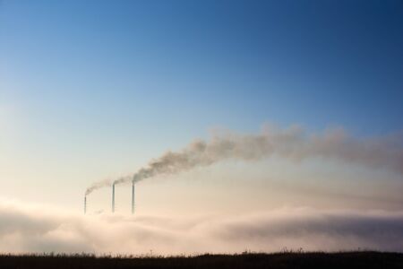 Tops of three smoking stacks of thermal power station on horizon taken from the hill, pipes in...