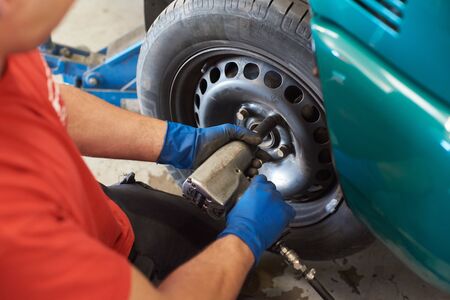 Close up of male hands in blue dirty gloves installing lug nuts. Professional mechanic using impact...