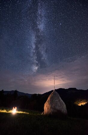 Natural landscape of valley hills with burning fire near haystack under the starry sky on which the Milky Way is visible. Beautiful night sky strewn with bright starsの写真素材