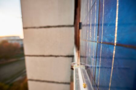 Close up of solar panel on window of a high-rise residential building against a background of a sleeping area of the city with clear blue sky on a warm day. Converting solar radiation into electricityの写真素材