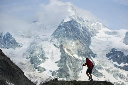 Male hiker climbing with hiking poles. Amazing, rocky mountain in snow in the Pennine Alps on...