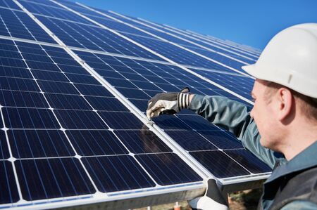 Close up of man technician mounting blue photovoltaic solar panel. Solar installer wearing safety helmet and gloves. Concept of alternative energy and power sustainable resources.の写真素材