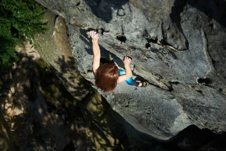 Horizontal snapshot of red haired woman in safety harness, climbing up the rock. Top view. Extreme sport conceptの写真素材