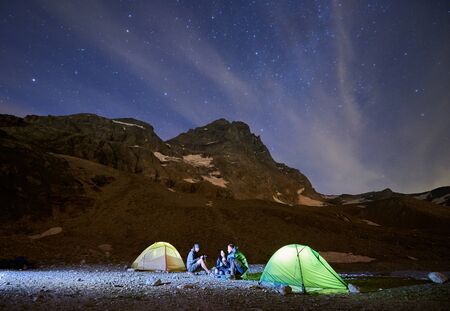 Magic scenery of blue cloudy sky and shining stars, beautiful mountains area. Three tourists...