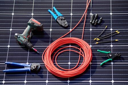 Close-up view of different details and instruments for mounting and connecting solar photovoltaic system. Objects laying on blue solar panel. Sustainable resources innovation environmental concept.の写真素材