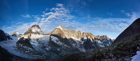 New day in the Swiss Alps, morning bright sun is shining at the ridge of rocky mountains Ober...