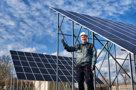 Man technician showing approval gesture thumbs up while standing near solar photovoltaic panel...