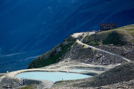 View of small lake with blue water in mountainous region. Silhouette of hiker walking on the shore....
