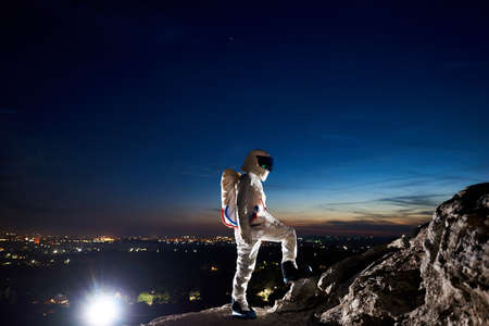 Full length of space traveler standing on rocky hill with blue night sky on background. Mission...