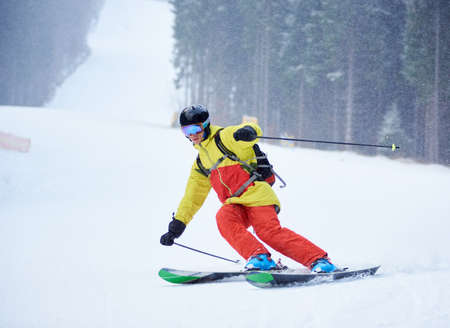 Front view of young male skier downhill skiing and doing carve turn on high snowy slope. Skiing...