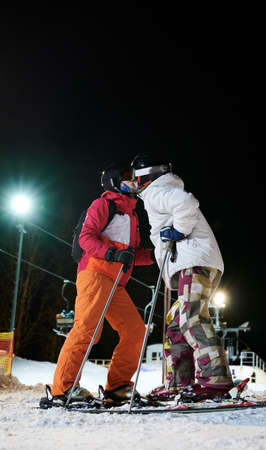 Side view of woman and man skiers kissing while spending time together at ski resort, standing on...