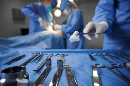 Close up of doctor hand holding forceps with tampon while surgeon and assistant performing plastic...