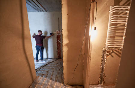 Rear view on young technician in empty unfinished apartment measuring the wall with a help of...