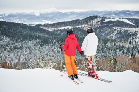 Back view of couple skiers wearing ski suits and ski equipment in winter mountains, enjoying snowy weather, skiing and incredible landscapes. Concept of winter sport activities, relationships.の写真素材