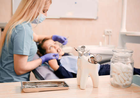 Close up of dental explorers, mirrors, scissors and scalers with pediatric dentist and little girl on blurred background. Stomatologist checking child teeth. Concept of dentistry, dental instruments.の写真素材