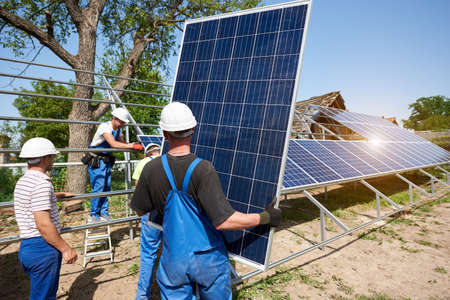 Team of four technicians working on exterior voltaic solar panel system installation in rural...