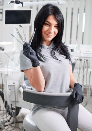 Female dentist in sterile gloves holding tools for dental treatment. Charming doctor smiling to camera while demonstrating dental instruments. Concept of dentistry, stomatology and dental medicine.の写真素材