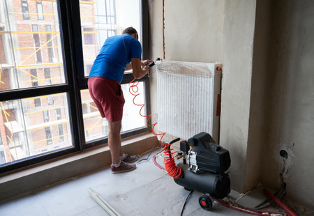 Back view of plumber filling pipes with pressurized air to inspect for leaks in new installation of heating system. Young man using air compressor. Concept of home renovation and gas tightness testingの写真素材
