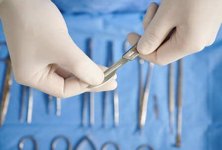 Close up view of doctors hands holding scalpel for plastic surgery. Surgeon with stainless steel...