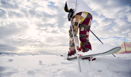 Close-up, low angle view snapshot of skiers legs wearing colorful ski pants and white jacket, making step forward on white snowy surface, ski tour. Copy space. Concept of winter sport activities.の写真素材