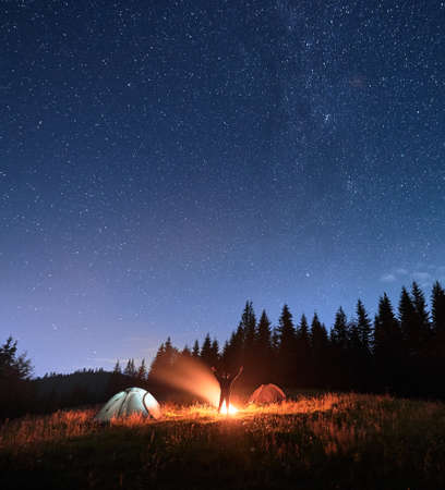 Male traveler standing near campfire and pointing at stars.の写真素材