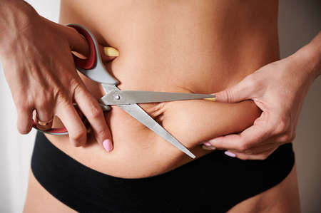 Young woman cutting off excess fat with scissors.の写真素材