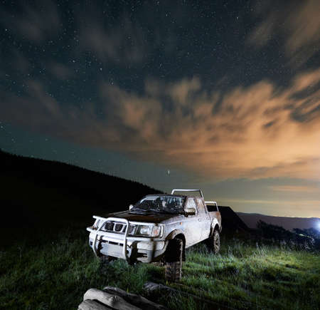 Dirty big car in the mountains at night. Concept of travelling, resting on nature and looking at starry sky with car.の写真素材