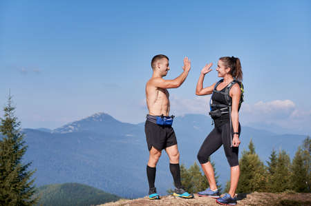 Good friends runners clapping each others hands when they reached top of mountain hill while extreme...