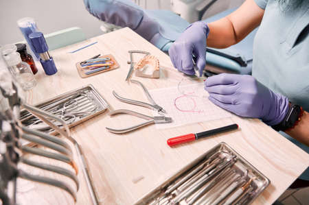 Close up view of female dentist in sterile gloves cutting braces wire while sitting at the table with orthodontic tools. Orthodontist preparing wire for braces attachment. Concept of dentistry.の写真素材