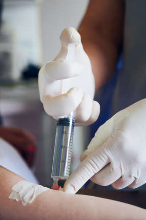 Close up of medical worker hands in sterile gloves injecting dose of anesthetic with syringe. Doctor inserting needle into patient arm while injecting anesthetic drug before surgery.の写真素材