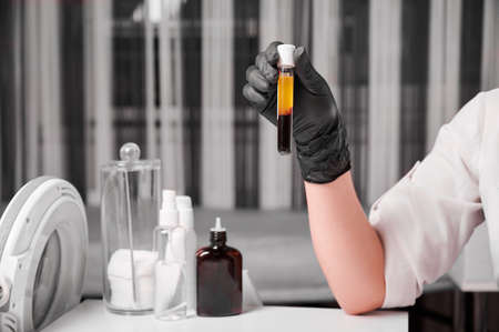 Close up of woman scientist hands in black gloves holding laboratory sample tube for blood. Female researcher preparing material for plasmolifting. Concept of clinical medicine.の写真素材